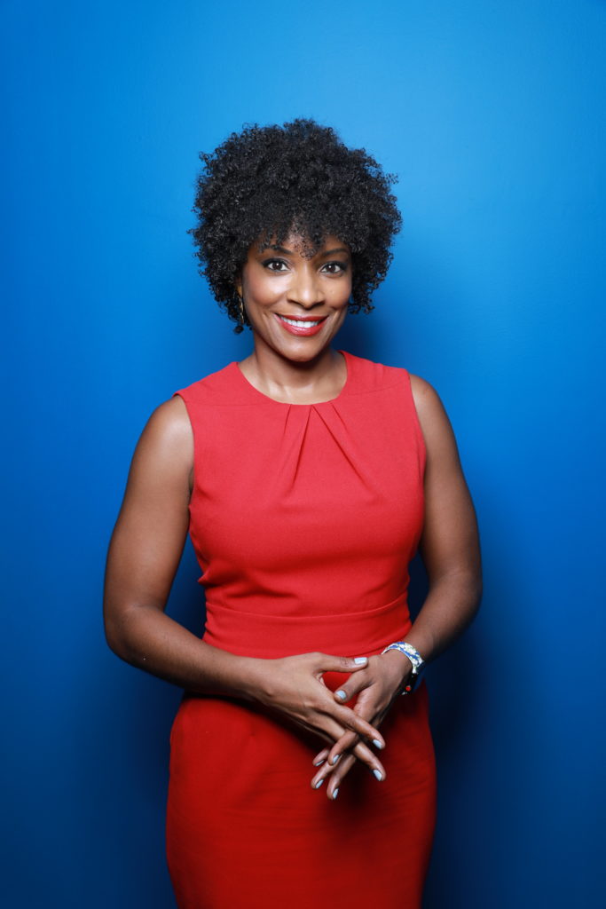 Zerlina Maxwell looks to camera, wearing a red dress in front of a blue background.